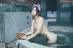 A naked woman sitting in a bathtub with a bowl of water.