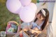 A woman sitting on a blanket with a basket of food and balloons.